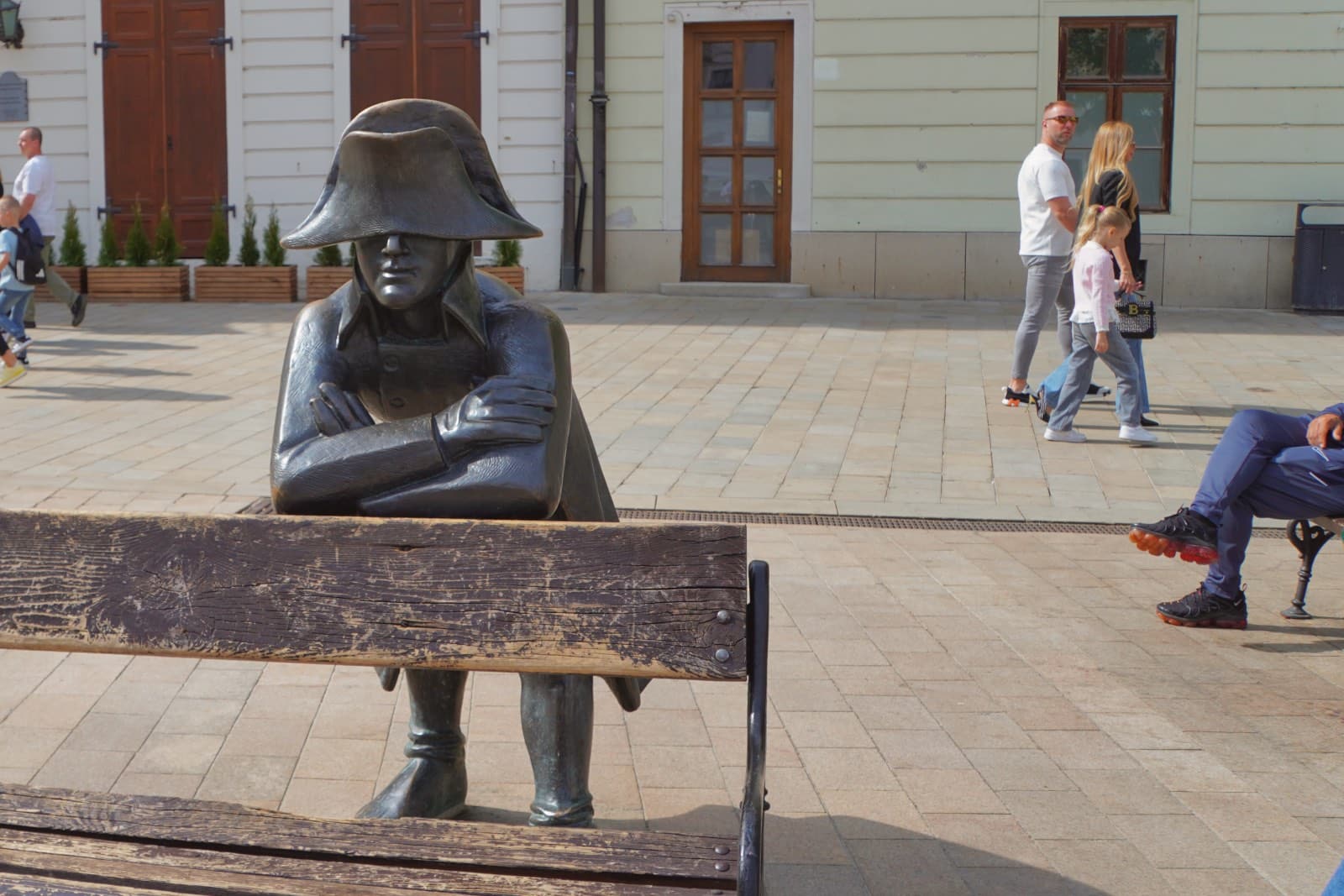 Eine Bronzeskulptur eines napoleonischen Soldaten lehnt mit verschränkten Armen an einer Holzbank