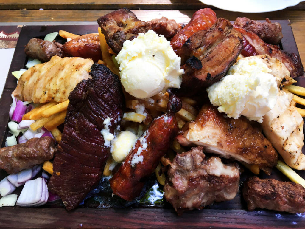 Eine reichhaltige gemischte Fleischplatte als preiswertes Hauptgericht in Belgrad, bestehend aus verschiedenen Grillspezialitäten wie Ćevapčići, Steaks, Würsten und Hähnchen, serviert mit Pommes Frites, Zwiebeln und zwei großen Kugeln Kajmak.