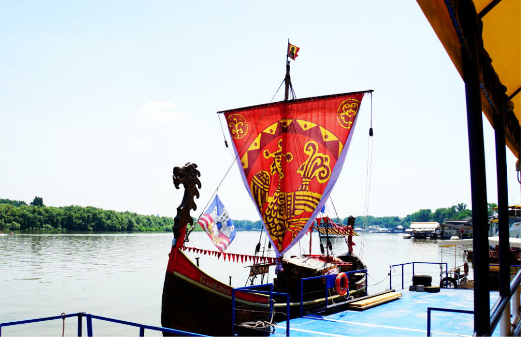 Ein nachgebautes Wikingerschiff mit rotem Segel und Drachenkopf liegt an einem Anleger in Belgrad, bereit für eine Fahrt über die Donau und Sava.