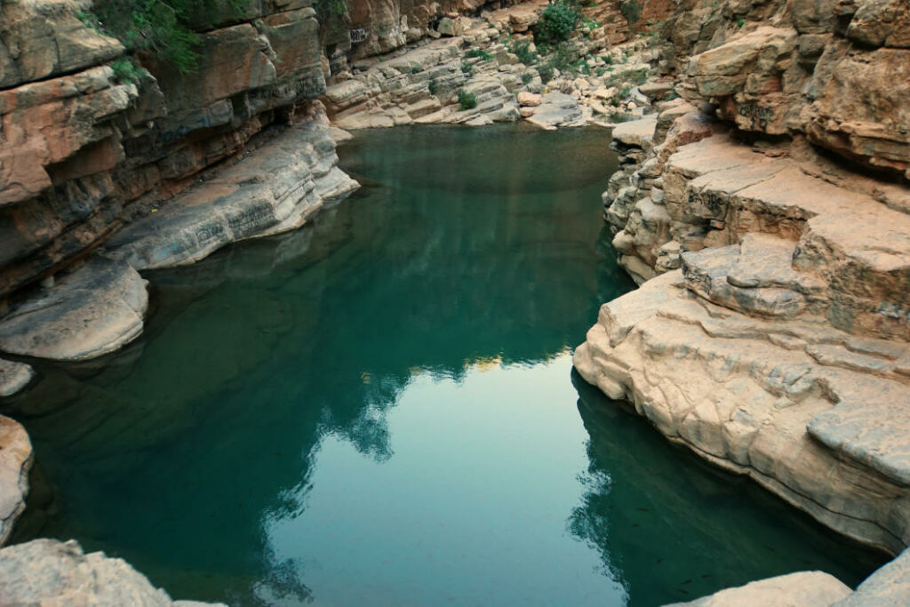 Ein klares, türkisfarbenes Felsenbecken schlängelt sich durch die steilen, geschichteten Felswände des Paradise Valley bei Agadir in Marokko.