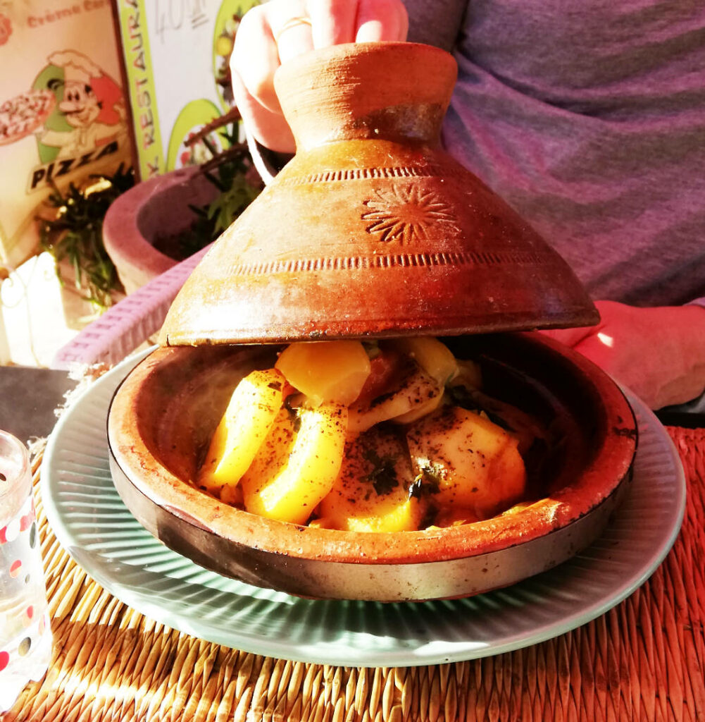 Eine traditionelle marokkanische Tajine aus Ton wird in Agadir serviert, wobei der kegelförmige Deckel angehoben wird, um gedünstete Kartoffeln und Gemüse zu enthüllen.