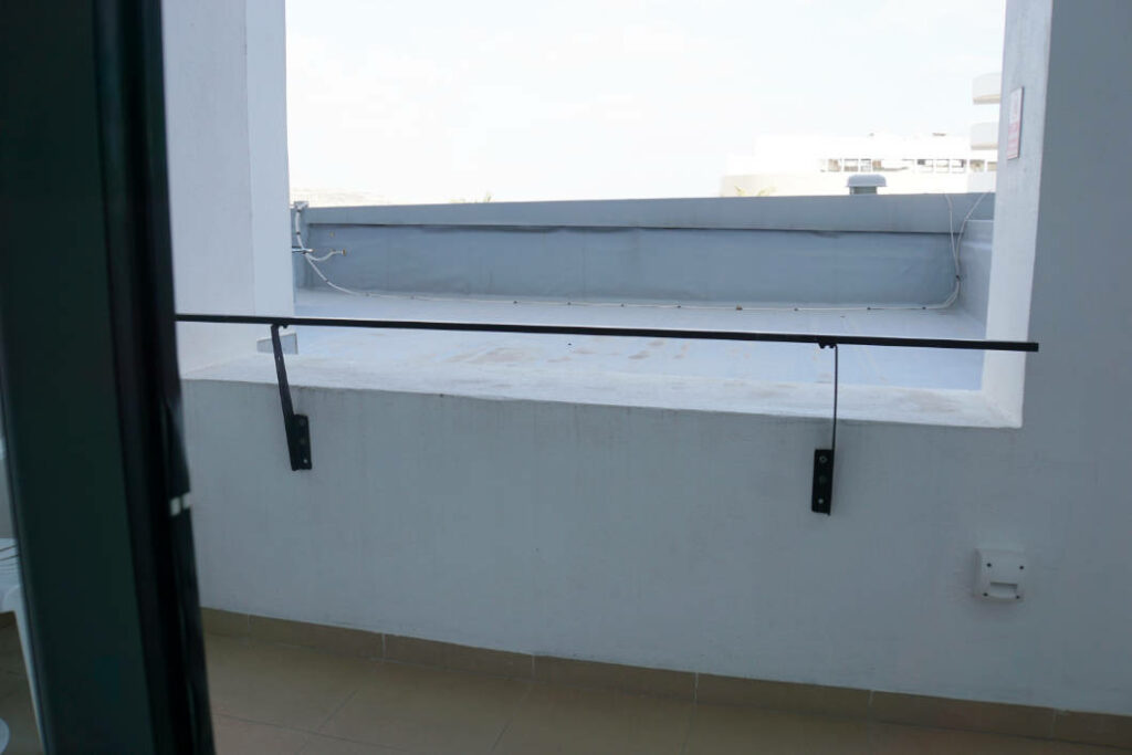 Blick von einem Balkon im 2. Stock eines Zimmers im db San Antonio Hotel + Spa auf Malta auf eine angrenzende Dachterrasse mit weißer Mauer und einfachem Metallgeländer.
