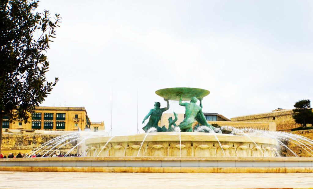 Der Tritonenbrunnen in Valletta, Malta, zeigt drei bronzene Tritonen, die eine große flache Schale über einem runden, wasserspeienden Becken emporheben.