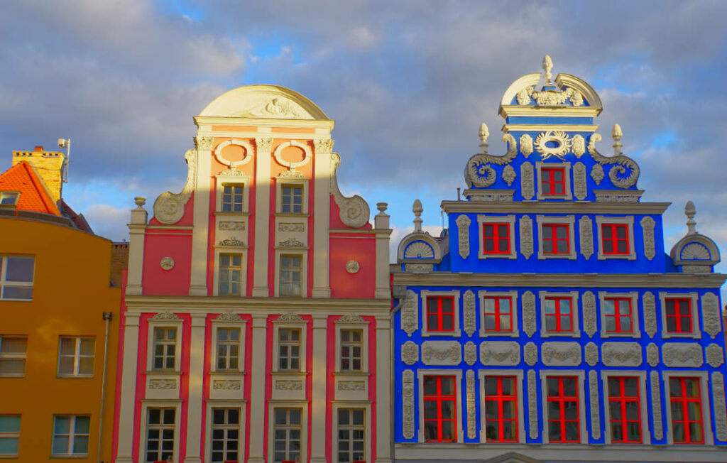 Zwei prächtig verzierte, farbenfrohe Giebelhäuser in Rosa und leuchtendem Blau am historischen Heumarkt in Stettin, die Teil des touristischen „Roten Wegs“ sind.