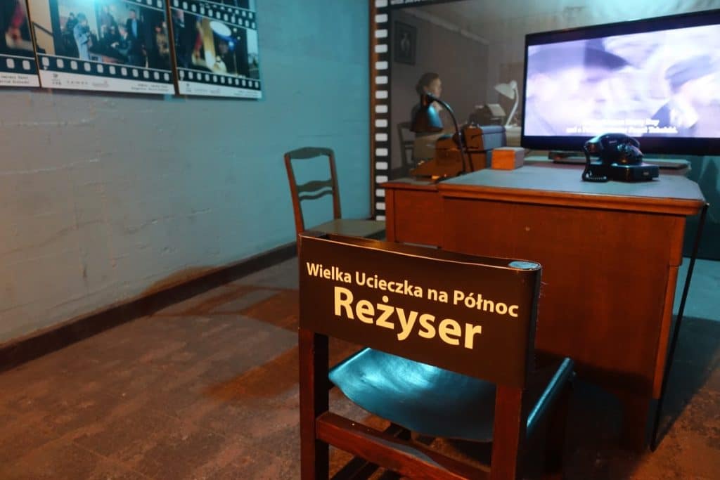 Ein nachgestelltes Filmset im Stettiner Bunker unter dem Hauptbahnhof zeigt einen Regiestuhl mit der Aufschrift „Wielka Ucieczka na Północ - Reżyser“ vor einem Schreibtisch mit altem Telefon und Monitor. Die Szenerie wird durch Filmstreifen-Plakate an der Wand und eine düstere Bunker-Atmosphäre ergänzt.