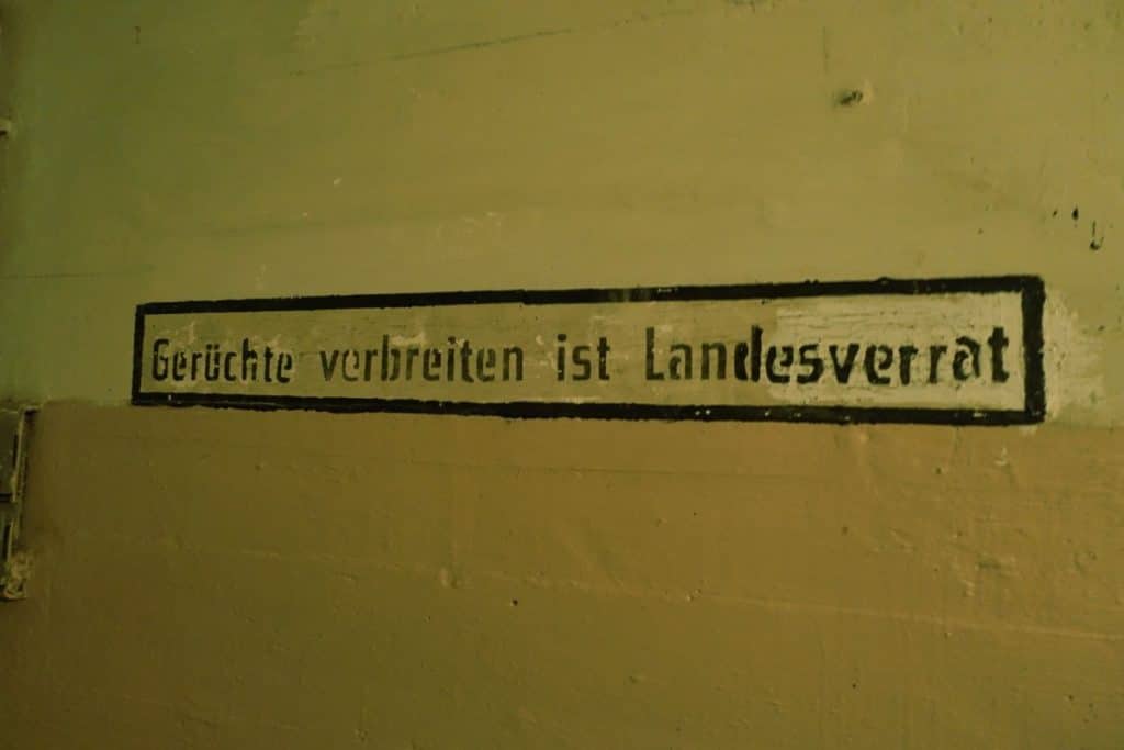 Eine historische Wandbeschriftung in einem Bunker unter dem Stettiner Hauptbahnhof mit der Aufschrift „Gerüchte verbreiten ist Landesverrat“ in schwarzer Frakturschrift auf hellem Grund.