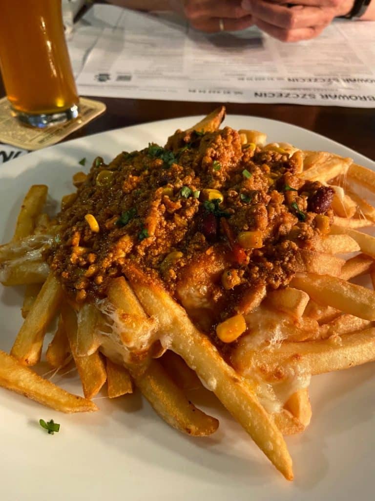 Ein Teller mit Chili-Cheese-Fries, getoppt mit Hackfleisch, Mais und geschmolzenem Käse, serviert mit einem Glas Bier in der Brauerei Nowy Browar in Stettin.