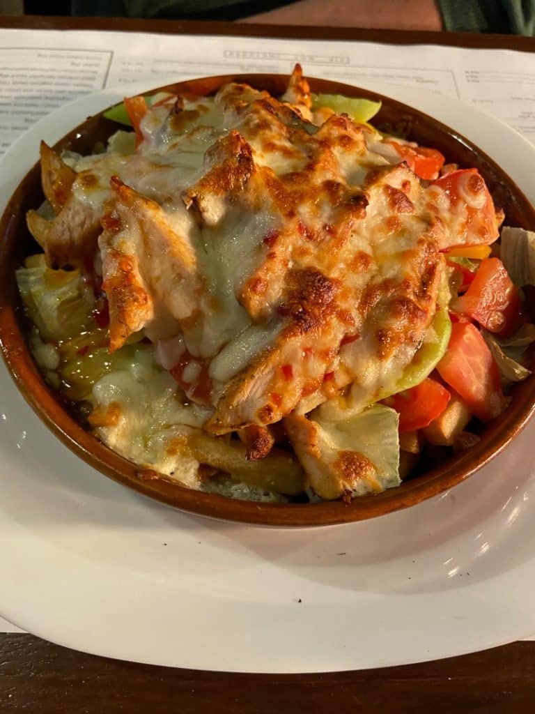 Ein herzhaftes Gericht in der Brauerei Nowy Browar in Stettin, bestehend aus mit Käse überbackenem Fleisch, Pommes frites und frischem Salat, serviert in einer Tonschale.