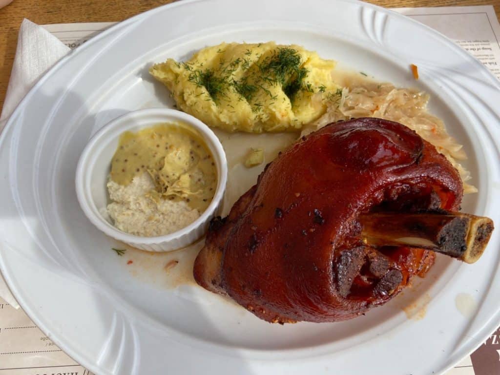 Eine gebratene Schweinshaxe der Brauerei Wyszak in Stettin, serviert auf einem weißen Teller mit Kartoffelstampf, Sauerkraut sowie Senf und Meerrettich in einem Schälchen.