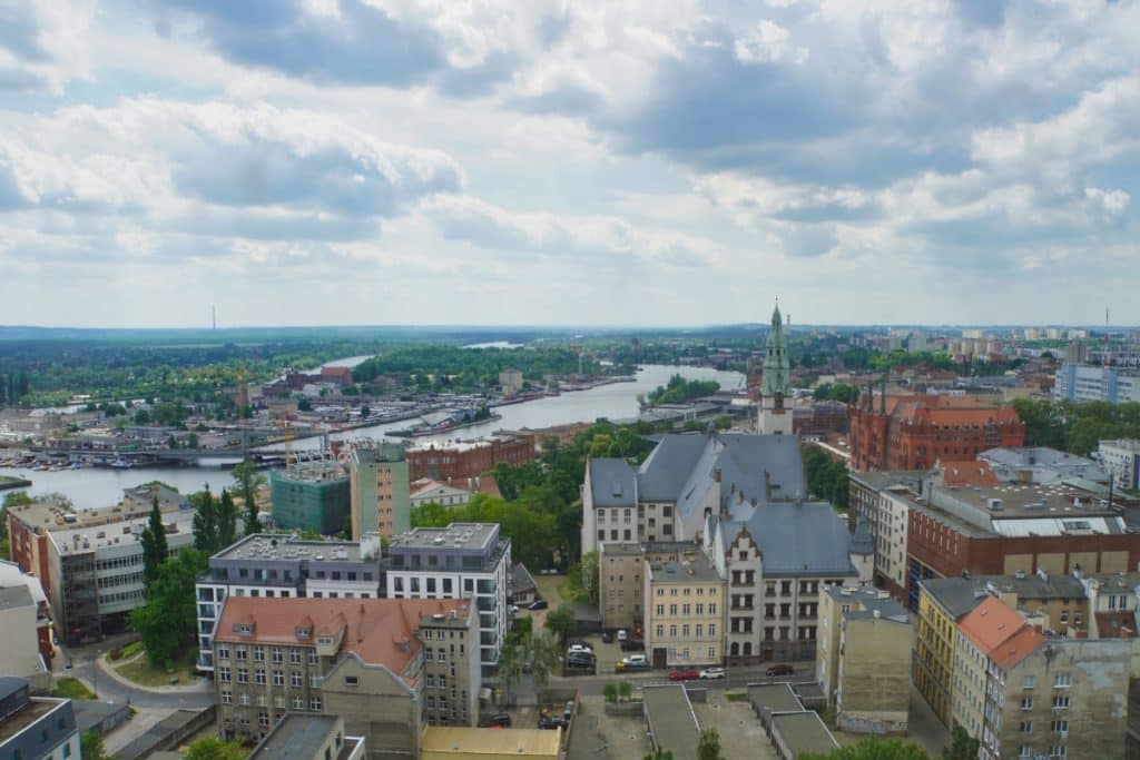 Blick von einem Aussichtspunkt in Stettin über die Stadtlandschaft mit der markanten St.-Jakobs-Kathedrale im Vordergrund und dem Fluss Oder, der in Richtung des Hauptbahnhofs fließt.