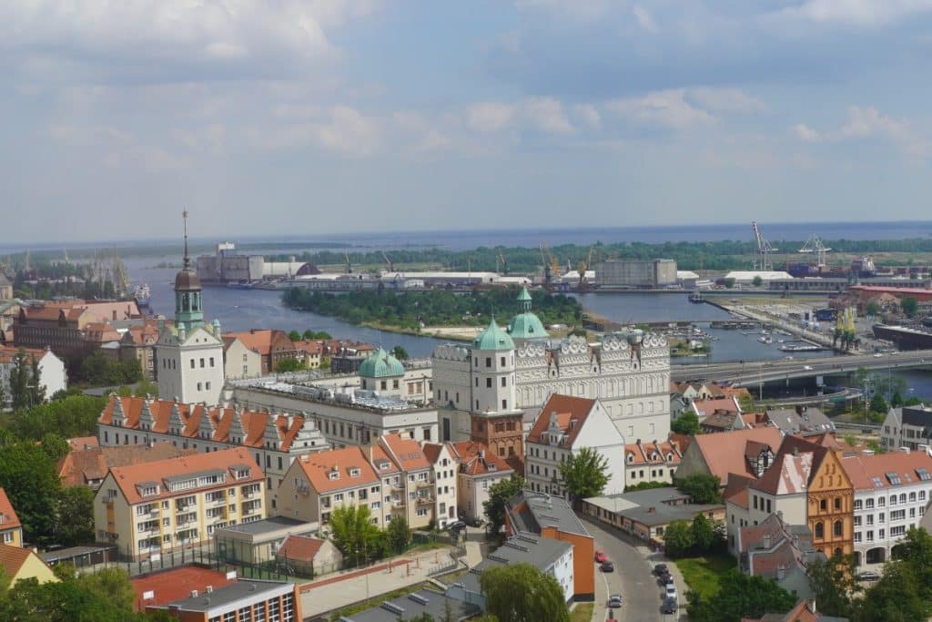 Blick von einem Aussichtspunkt über die Dächer von Stettin auf das imposante Herzogsschloss mit seinen markanten grünen Türmen und die dahinterliegende Oder mit dem Hafenareal.