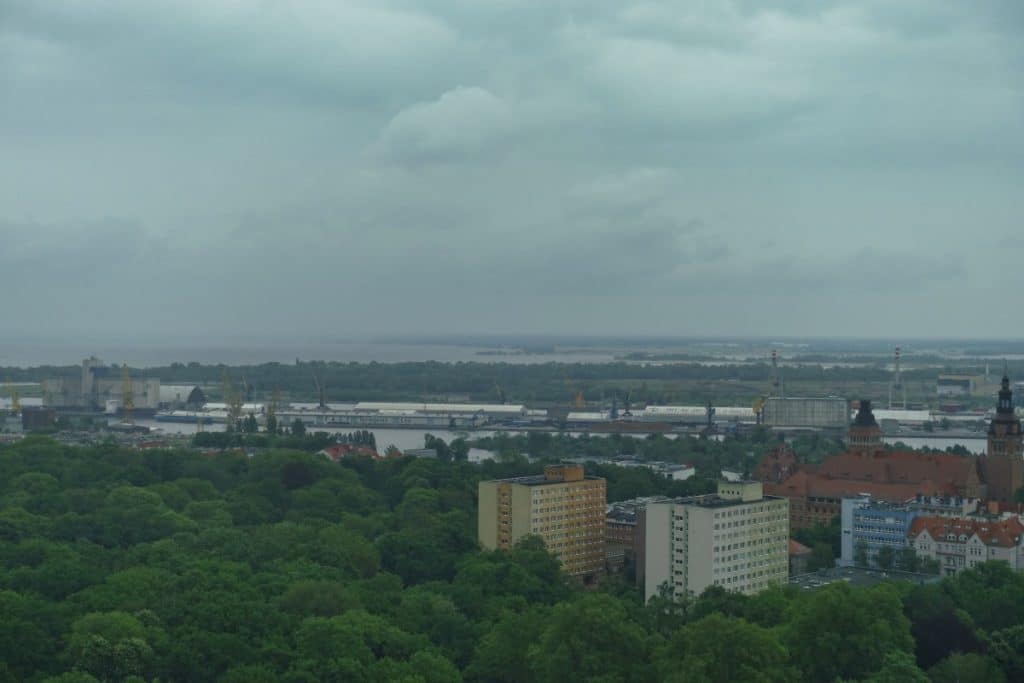 Blick vom Café 22 über die grüne Stadtlandschaft von Stettin auf den Hafen und die Oder unter einem bewölkten Himmel.