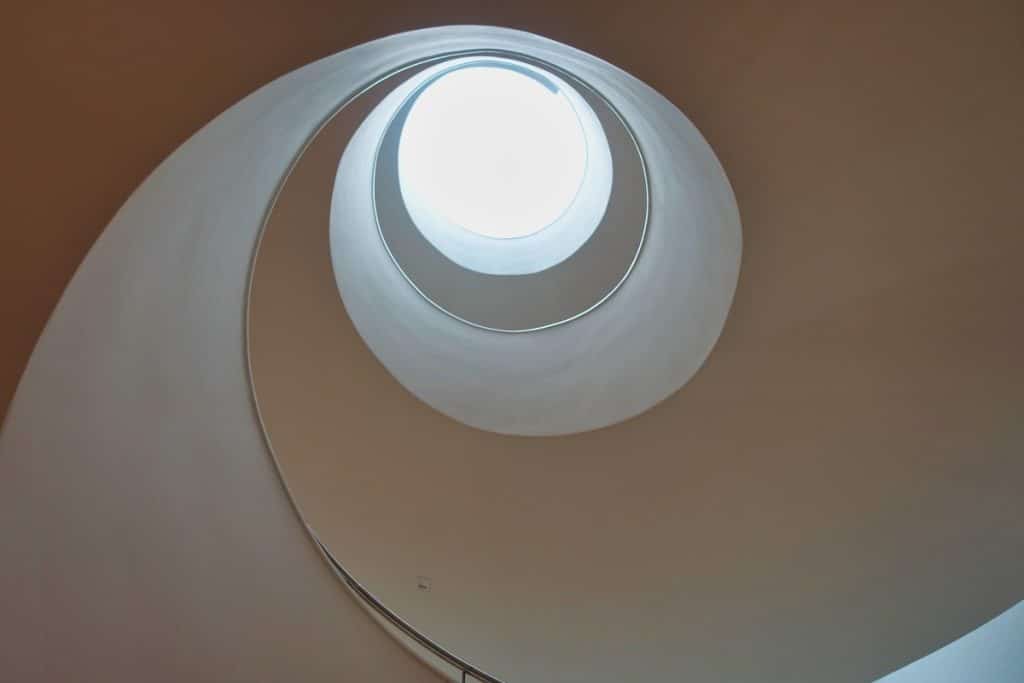 Blick von unten in das spiralförmige, weiße Treppenauge der Philharmonie Stettin, das in einem runden Oberlicht gipfelt.
