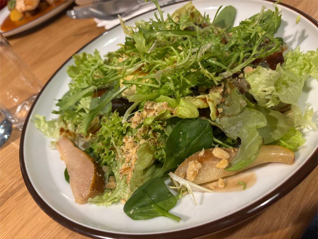 Ein frischer gemischter Salat mit Blattsalat, Rucola, Birnenspalten und Nüssen, serviert auf einem weißen Teller im Restaurant Na Spilce in Pilsen.