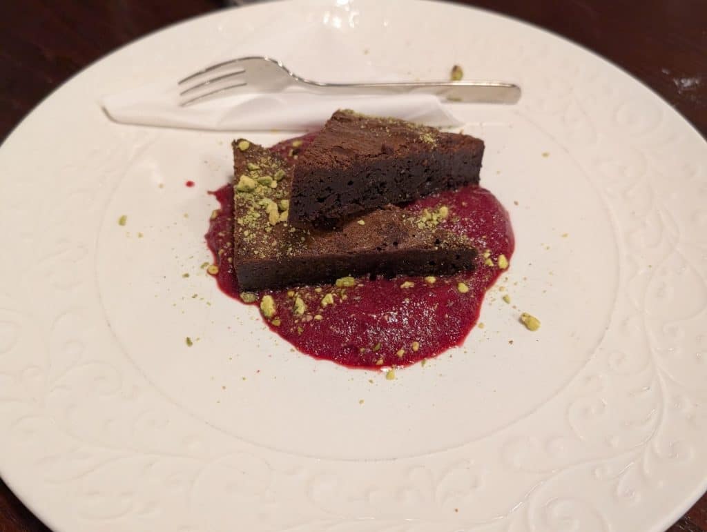 Ein Schokoladen-Brownie mit Pistazienkernen auf einem Fruchtspiegel, serviert im Restaurant Purkmistr in Pilsen.