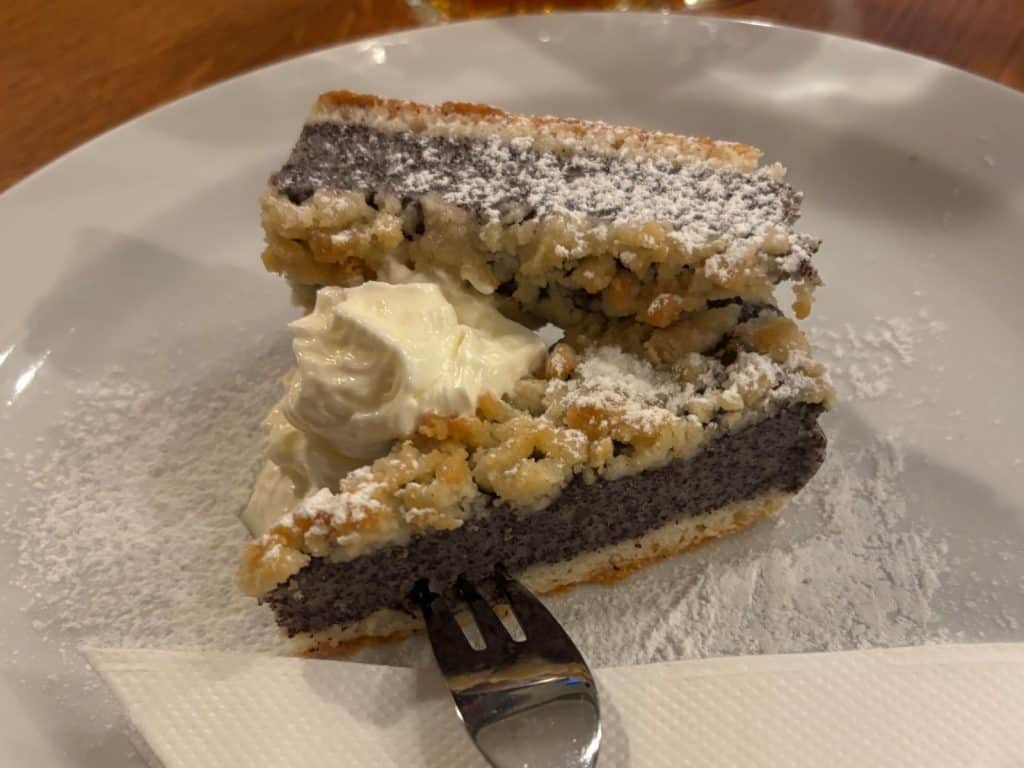 Ein Stück traditioneller tschechischer Mohnkuchen mit Streuseln, Puderzucker und einem Klecks Sahne, serviert auf einem weißen Teller im Restaurant U Salzmannů in Pilsen.