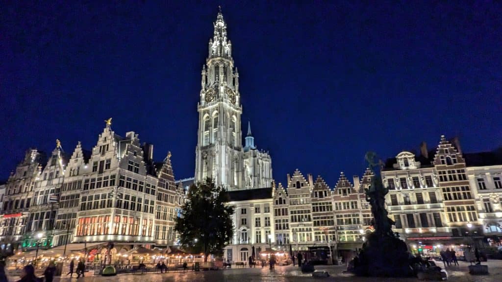 Beleuchtete Gildehäuser mit Treppengiebeln säumen den abendlichen Grote Markt in Antwerpen, überragt vom prachtvoll illuminierten Turm der Liebfrauenkathedrale unter einem tiefblauen Nachthimmel.