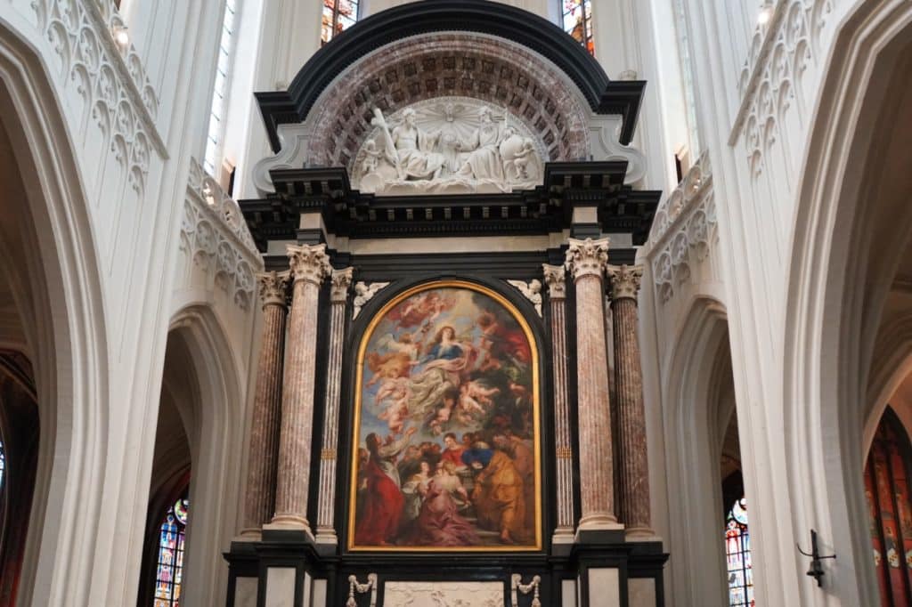 Der prunkvolle Hochaltar zeigt Peter Paul Rubens’ Gemälde „Mariä Himmelfahrt“, das von monumentalen Marmorsäulen und einer skulpturalen Darstellung der Heiligen Dreifaltigkeit eingerahmt wird.