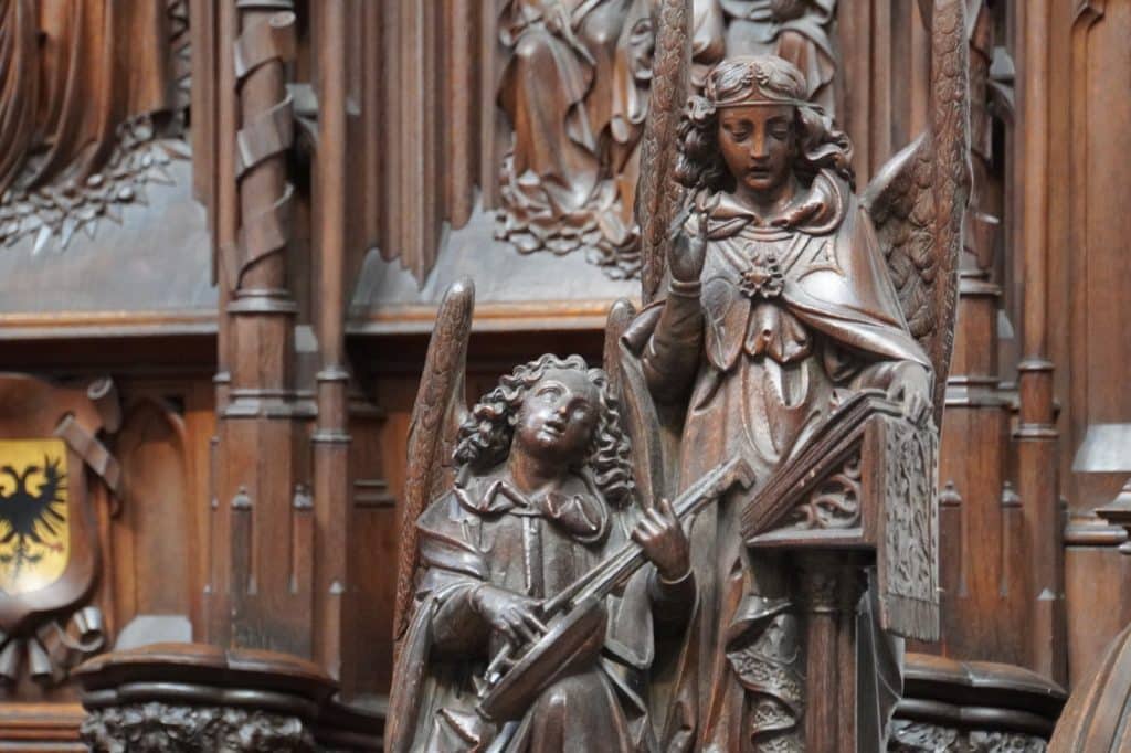 Detailreiche Holzschnitzerei am Chorgestühl der Liebfrauenkathedrale von Antwerpen, die zwei Engel zeigt, von denen einer ein Saiteninstrument spielt und der andere an einem Lesepult steht.