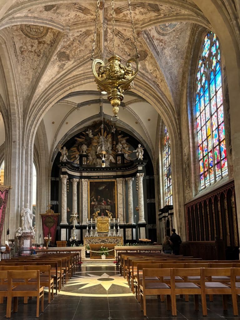 Blick in eine Seitenkapelle der Liebfrauenkathedrale von Antwerpen mit einem prunkvollen Barockaltar, kunstvollen Deckenfresken und einem großen, farbenfrohen Buntglasfenster auf der rechten Seite.