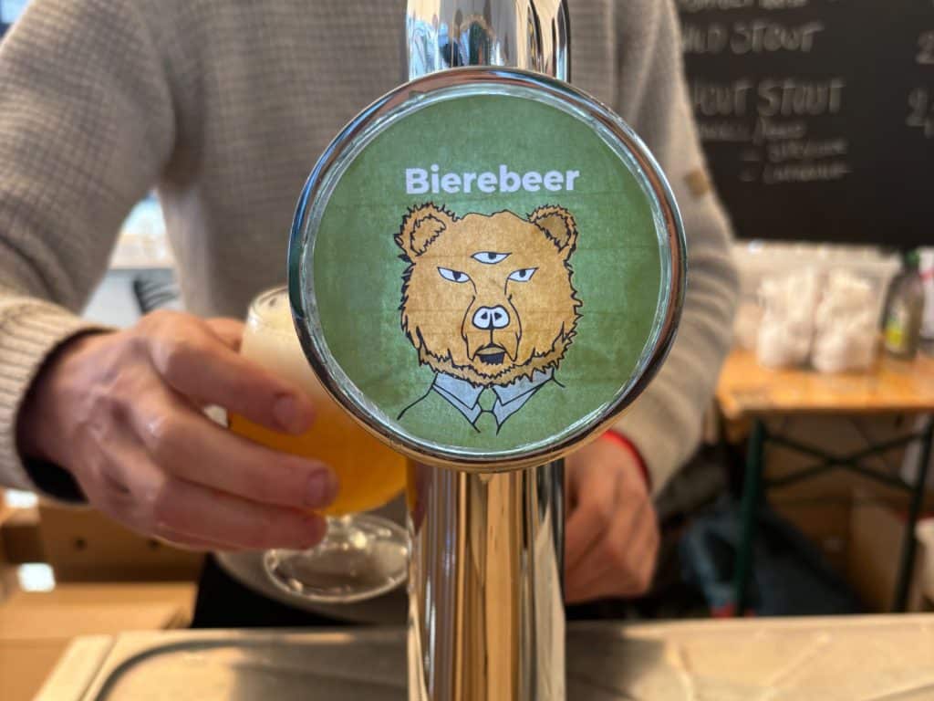 Nahaufnahme eines Zapfhahns beim Antwerpen Bier Festival mit einem runden Logo, das den Schriftzug „Bierebeer“ und einen dreiäugigen Bären im Anzug auf grünem Hintergrund zeigt.
