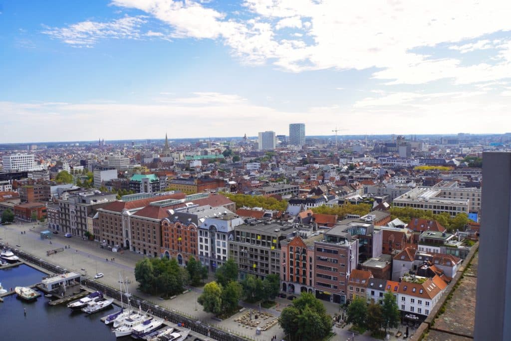 Blick vom Museum aan de Stroom (MAS) über das Stadtpanorama von Antwerpen mit dem Hafenbecken im Vordergrund und dem historischen Stadtzentrum unter einem leicht bewölkten Himmel.