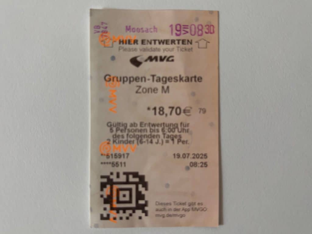 Ein Foto eines entwerteten MVG-Gruppen-Tagestickets für den Münchner öffentlichen Nahverkehr (Zone M), das am Bahnhof Moosach abgestempelt wurde. Das Ticket zeigt Details wie den Preis von 18,70 €, die Gültigkeit für bis zu 5 Personen und einen QR-Code im unteren Bereich.