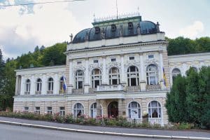 Außenansicht des neobarocken Casino in Marienbad mit einer kunstvollen Fassade, Statuen auf dem Dachgesims und einem gepflegten Rosengarten im Vordergrund.