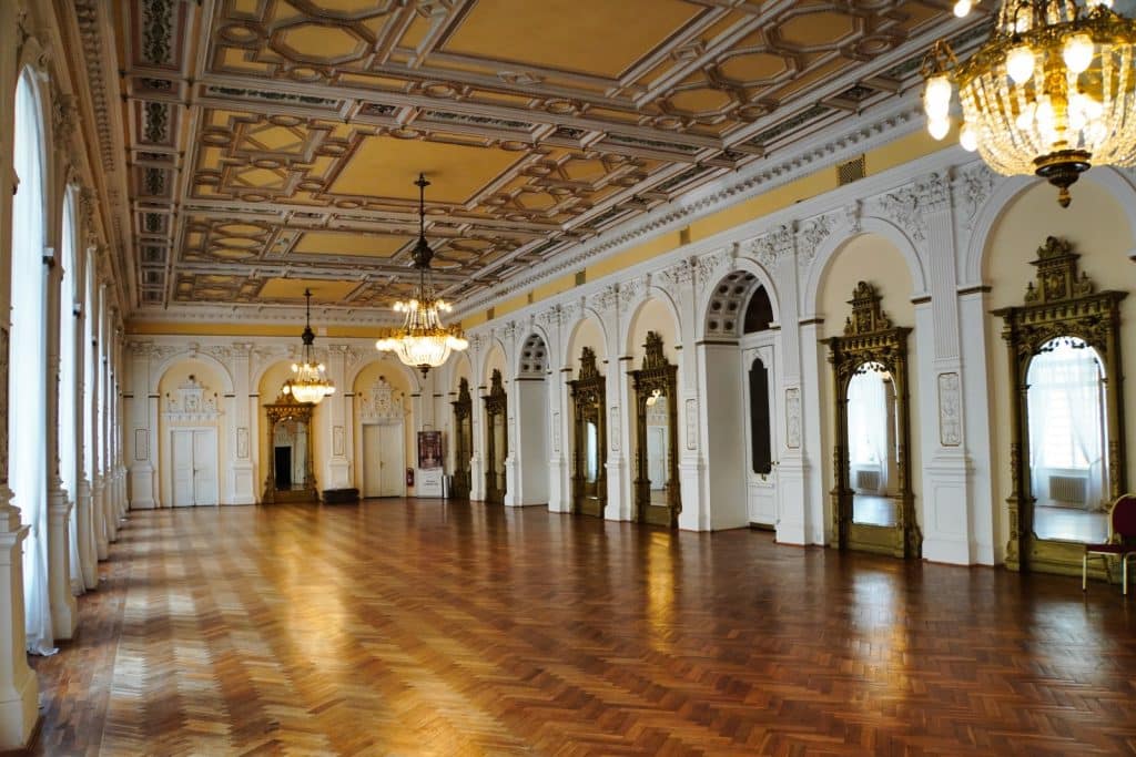 Der prachtvolle Spiegelsaal im Casino von Marienbad besticht durch ein kunstvolles Fischgrätparkett, eine reich verzierte Kassettendecke und goldgerahmte Spiegelwände, die von eleganten Kronleuchtern beleuchtet werden.