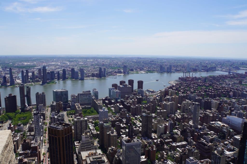 Weitläufiger Blick von der Aussichtsplattform des Empire State Building über die dichte Wolkenkratzer-Landschaft New Yorks bis hin zum East River und den gegenüberliegenden Stadtteilen.