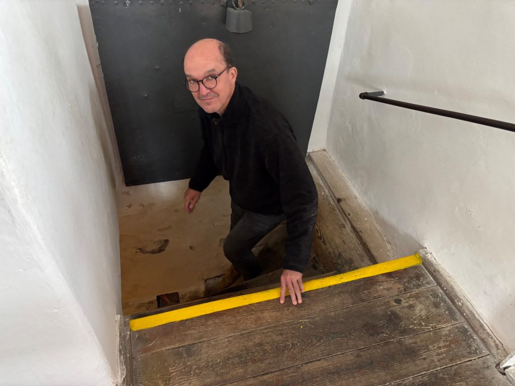 Ein Mann mit Brille und schwarzer Jacke steigt eine schmale Holztreppe im Schwarzen Turm in Klattau hinunter.