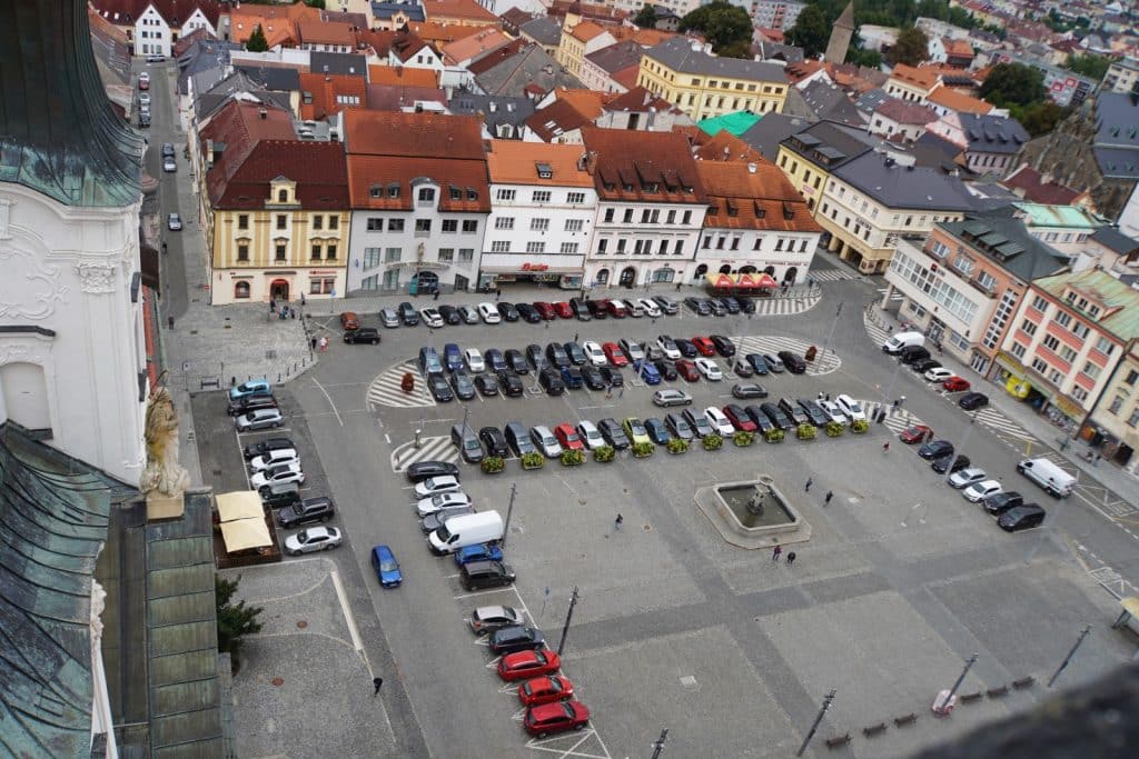 Blick von oben auf den Marktplatz von Klattau (Klatovy) mit einem zentralen Brunnen und den umliegenden historischen Gebäuden mit roten Ziegeldächern.