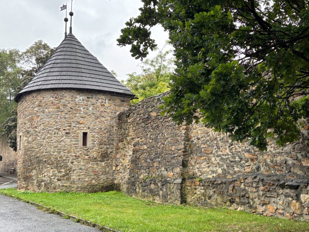 Ein runder Wehrturm mit kegelförmigem Schindeldach und schmalen Schießscharten ist Teil der historischen Stadtmauer von Klattau, die aus grobem Naturstein gemauert ist.