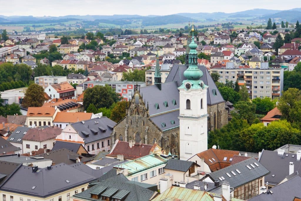 Blick über die Dächer von Klattau auf die Stadtpfarrkirche Mariä Geburt und den markanten Weißen Turm mit seiner grünen Zwiebelhaube vor einer hügeligen Landschaft.