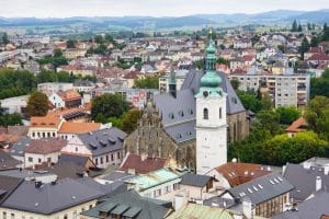 Blick über die Dächer von Klattau auf die Stadtpfarrkirche Mariä Geburt und den markanten Weißen Turm mit seiner grünen Zwiebelhaube vor einer hügeligen Landschaft.
