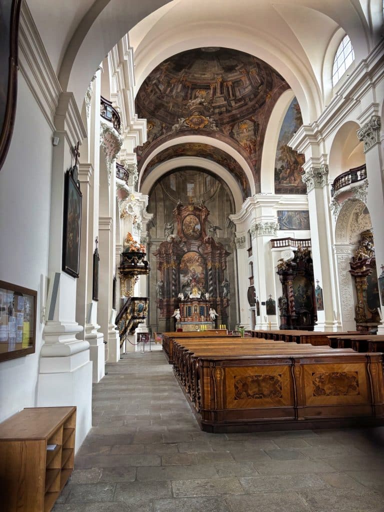 Innenansicht der Jesuitenkirche in Klattau mit Blick durch das helle Kirchenschiff auf den prunkvollen Hochaltar und die kunstvoll bemalte Kuppel über den hölzernen Kirchenbänken.