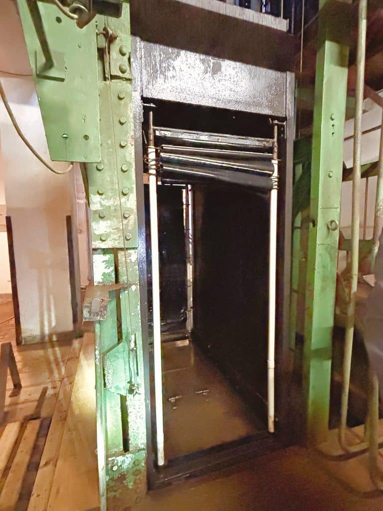 Ein historischer, offener Förderkorb eines Bergwerksaufzugs in Ehrenfriedersdorf, Sachsen, mit grünen Metallstreben und einer dunklen Kabine.