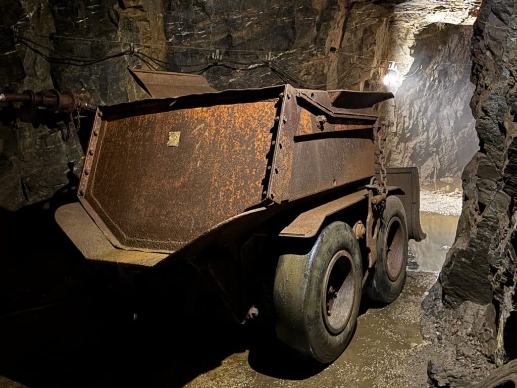 Ein rostiges, historisches Bergbaufahrzeug mit großen Gummireifen steht in einem dunklen, felsigen Stollen des Besucherbergwerks in Ehrenfriedersdorf, Sachsen.