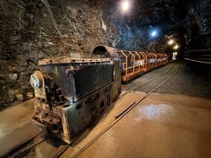 Eine historische Grubenbahn mit einer rostigen Lokomotive und mehreren orangefarbenen Personenwagen steht auf Schienen in einem beleuchteten Stollen der Zinnerzgrube in Ehrenfriedersdorf, Sachsen.
