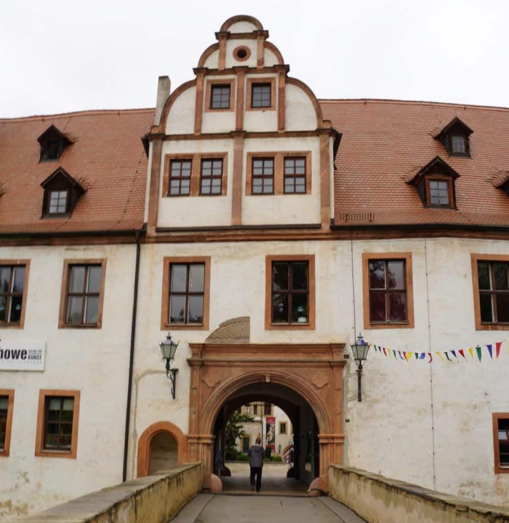Ein Mann geht über eine Brücke auf den Torbogen des historischen Schlosses Forderglauchau in Glauchau, Sachsen, zu, das durch seine weiße Fassade und den markanten Renaissance-Giebel besticht.