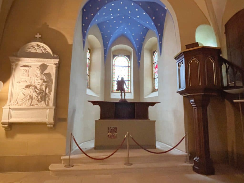 Blick in die Kapelle von Schloss Glauchau in Sachsen mit einem schlichten Altar vor einem blauen Sternengewölbe, flankiert von einem weißen Wandrelief und einer hölzernen Kanzel.