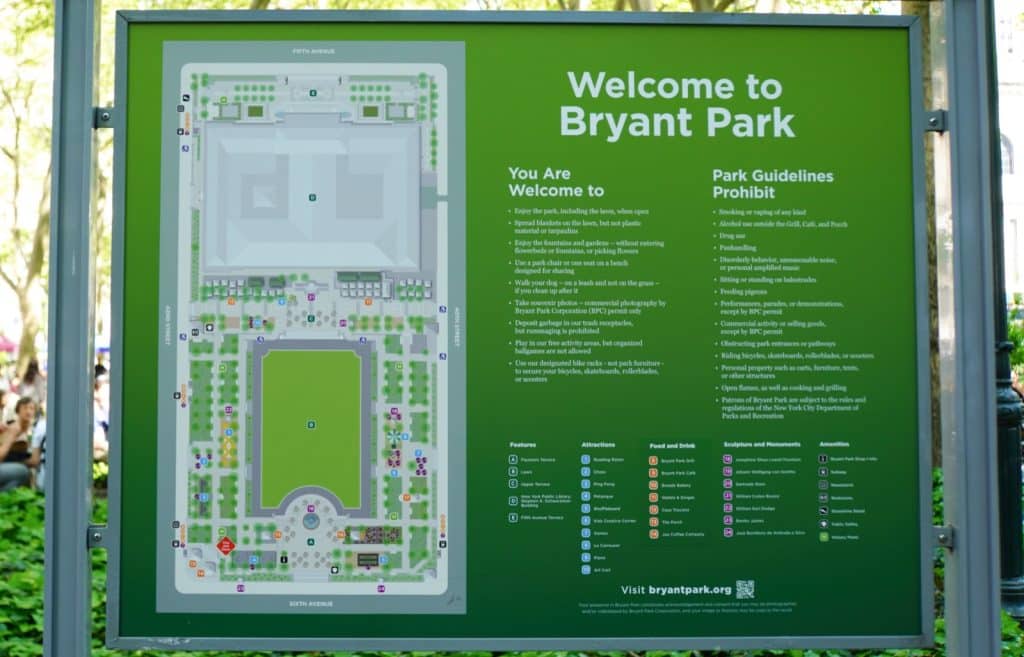 Ein grünes Hinweisschild zeigt einen detaillierten Lageplan des Bryant Park in New York sowie eine Liste mit Parkregeln und Legenden zu Attraktionen, Gastronomie und Denkmälern.