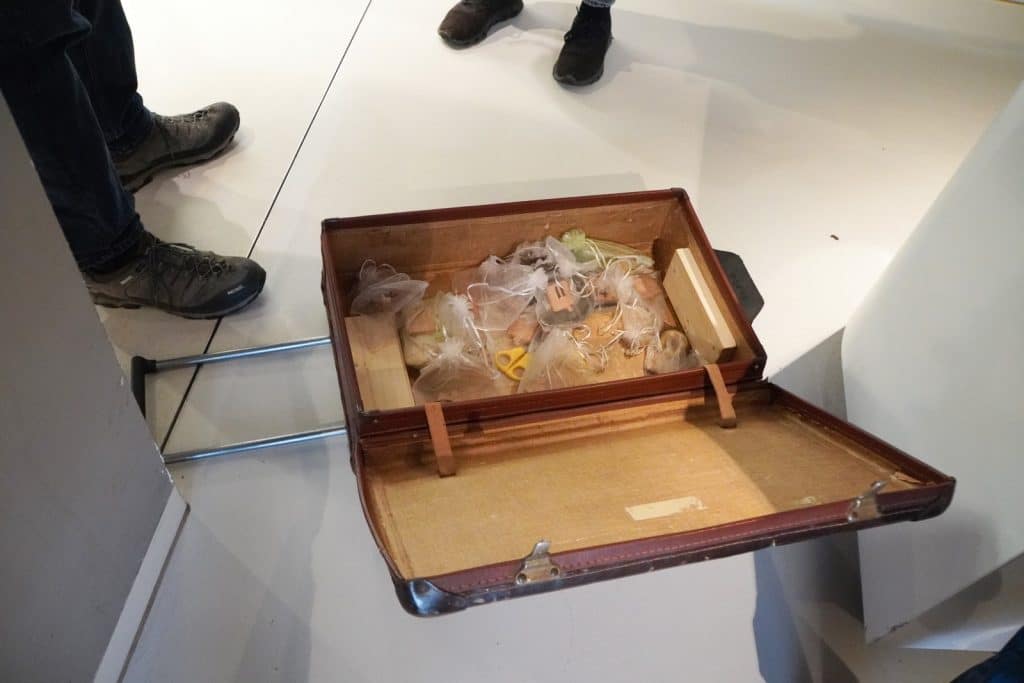 Ein offener, brauner Vintage-Koffer für Kinder im Museum Hoge Woerd liegt auf dem Boden und enthält verschiedene kleine, in weißen Säckchen verpackte Gegenstände sowie Holzelemente.