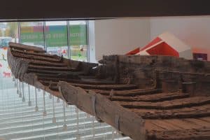 Das antike römische Holzschiff „De Meern 1“ ist im Museum Castellum Hoge Woerd in Utrecht ausgestellt und wird von einer modernen Metallkonstruktion über einem hellen Ausstellungsraum getragen.