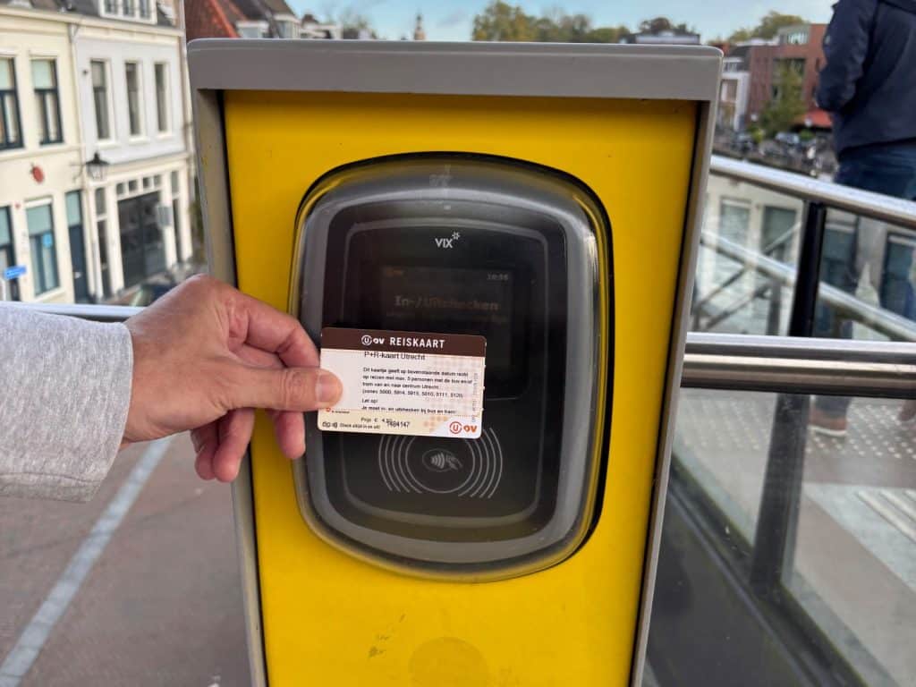 Eine Hand hält eine braune OV-Reisekarte an ein gelbes Lesegerät zum Einchecken in den öffentlichen Nahverkehr in Utrecht.