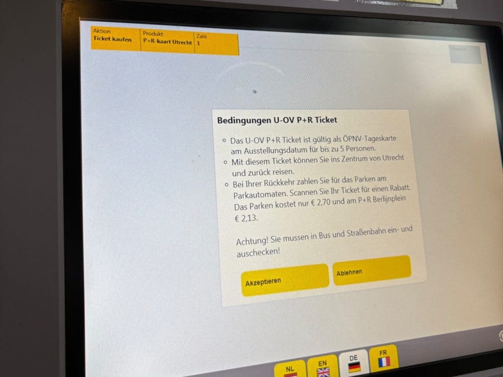 Ein Parkautomat in Utrecht zeigt auf seinem Bildschirm die Bedingungen für ein „U-OV P+R Ticket“ auf Deutsch an, mit Schaltflächen zum Akzeptieren oder Ablehnen. Der Text informiert über die Gültigkeit als ÖPNV-Tageskarte für bis zu 5 Personen und die Rabattierung der Parkgebühren bei Rückkehr.