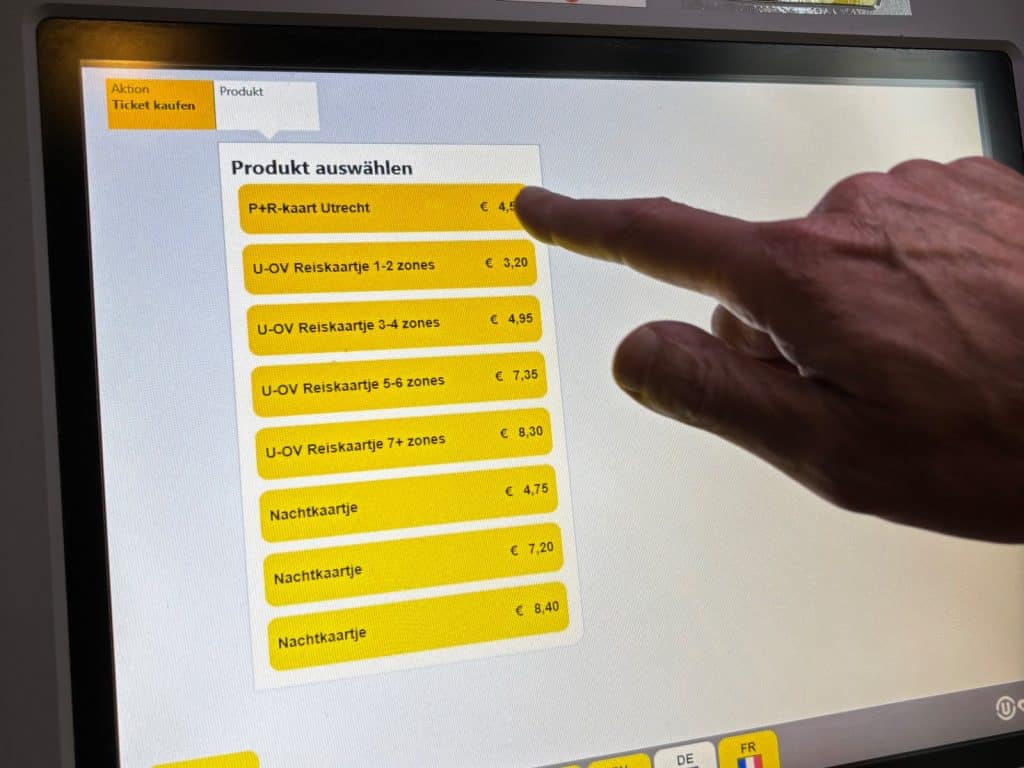 Eine Hand wählt auf dem Touchscreen eines Ticketautomaten in Utrecht das „P+R-kaart Utrecht“ für 4,50 € aus einer Liste verschiedener Fahrkartenoptionen aus.