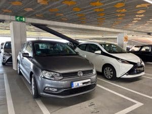 Ein grauer Volkswagen und ein weißer Toyota parken nebeneinander in einem Parkhaus in Utrecht, dessen Decke mit gelben Ginkgoblatt-Mustern verziert ist.