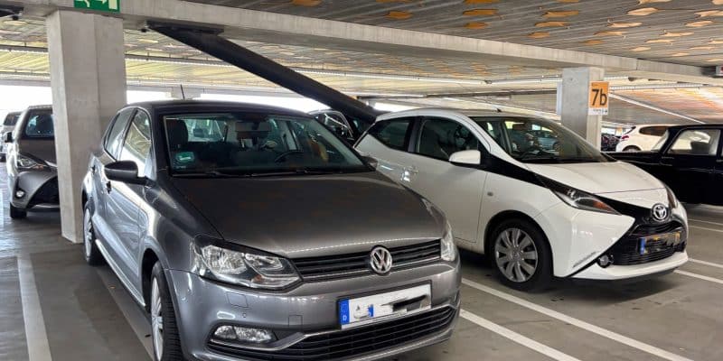 Ein grauer Volkswagen und ein weißer Toyota parken nebeneinander in einem Parkhaus in Utrecht, dessen Decke mit gelben Ginkgoblatt-Mustern verziert ist.