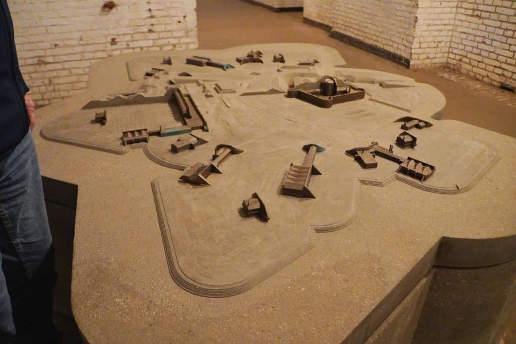 Ein detailliertes, sandfarbenes Reliefmodell der Verteidigungsanlagen der Utrechter Wasserlinie steht in einem Raum mit hellen Ziegelwänden. Das Modell zeigt verschiedene Festungsbauten, Gräben und Erdwälle in einer weitläufigen, sternförmigen Anordnung.